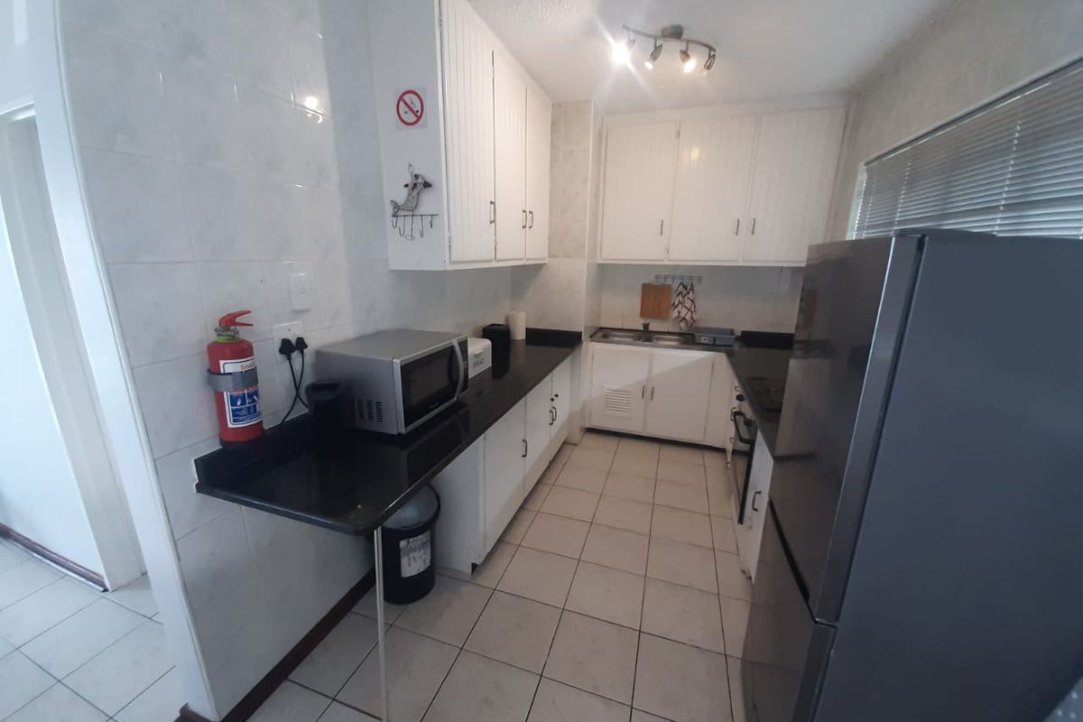 A functional galley-style kitchen featuring white cabinetry, dark countertops, tiled walls, and ceramic floor tiles.