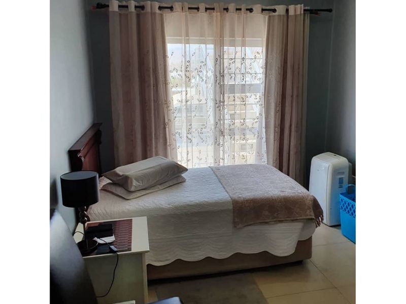 A functional bedroom featuring tiled flooring and a large window with curtain fixtures, providing a neutral base for interior design updates.