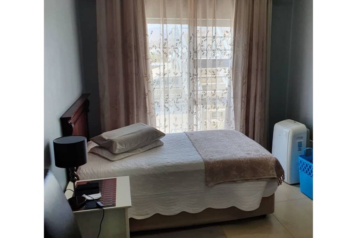 A functional bedroom featuring tiled flooring and a large window with curtain fixtures, providing a neutral base for interior design updates.