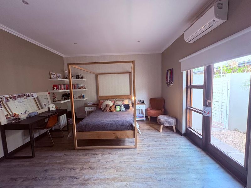 Spacious bedroom featuring timber-look flooring, recessed lighting, a split-system air conditioner, and direct access to an outdoor area through sliding glass doors.