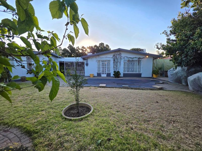Rear view of the house featuring a paved patio area, security bars on windows, and a garden with a lawn.