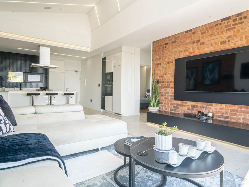 Modern open-plan living area featuring an exposed brick wall, sleek kitchen cabinetry, integrated appliances, and high ceilings with recessed lighting.