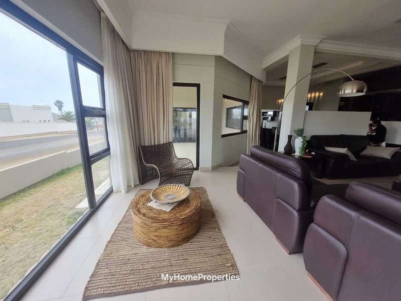 Spacious open-plan living area featuring large windows, tiled flooring, and modern architectural ceiling details, offering a bright and airy atmosphere.