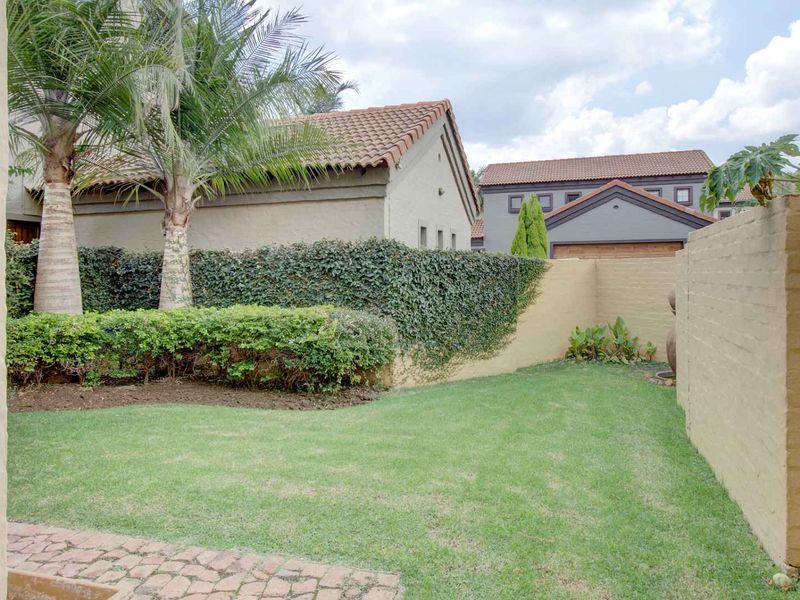 A private rear garden featuring a well-maintained lawn, paved patio area, and established boundary walls with ivy coverage.