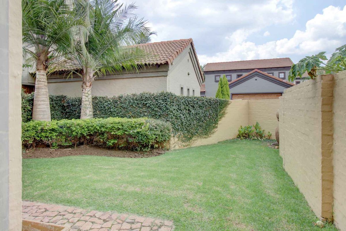 A private rear garden featuring a well-maintained lawn, paved patio area, and established boundary walls with ivy coverage.