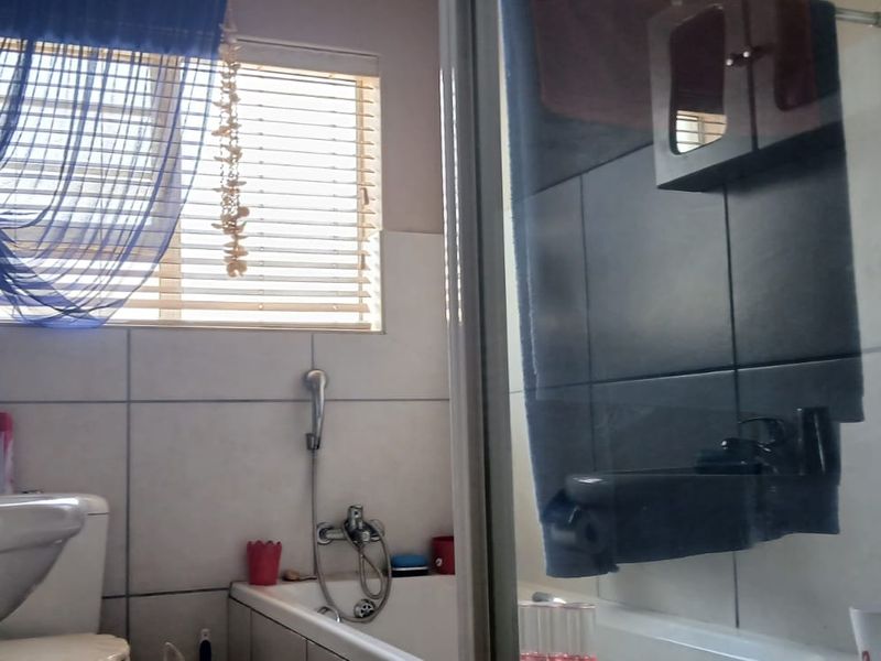 A functional bathroom featuring a bathtub, separate shower enclosure, pedestal basin, and toilet, finished with neutral wall tiling and window blinds.