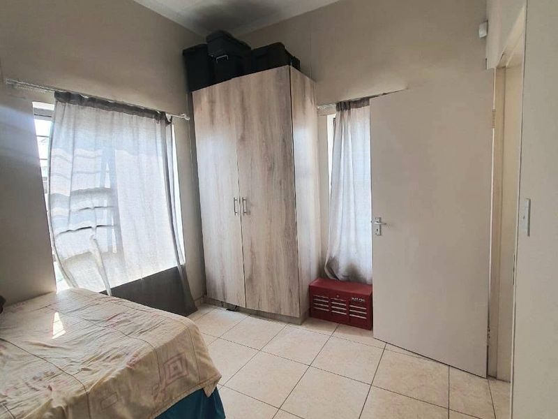 A functional bedroom featuring neutral tiled flooring and a built-in wardrobe, offering a clean and practical living space.