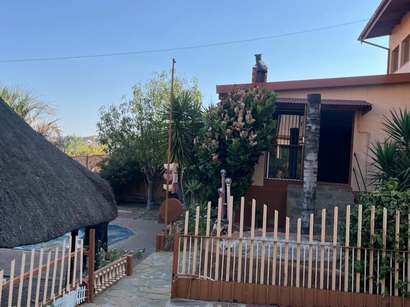 Rear exterior view featuring a thatch roof lapa, swimming pool, paved patio area, and perimeter fencing.