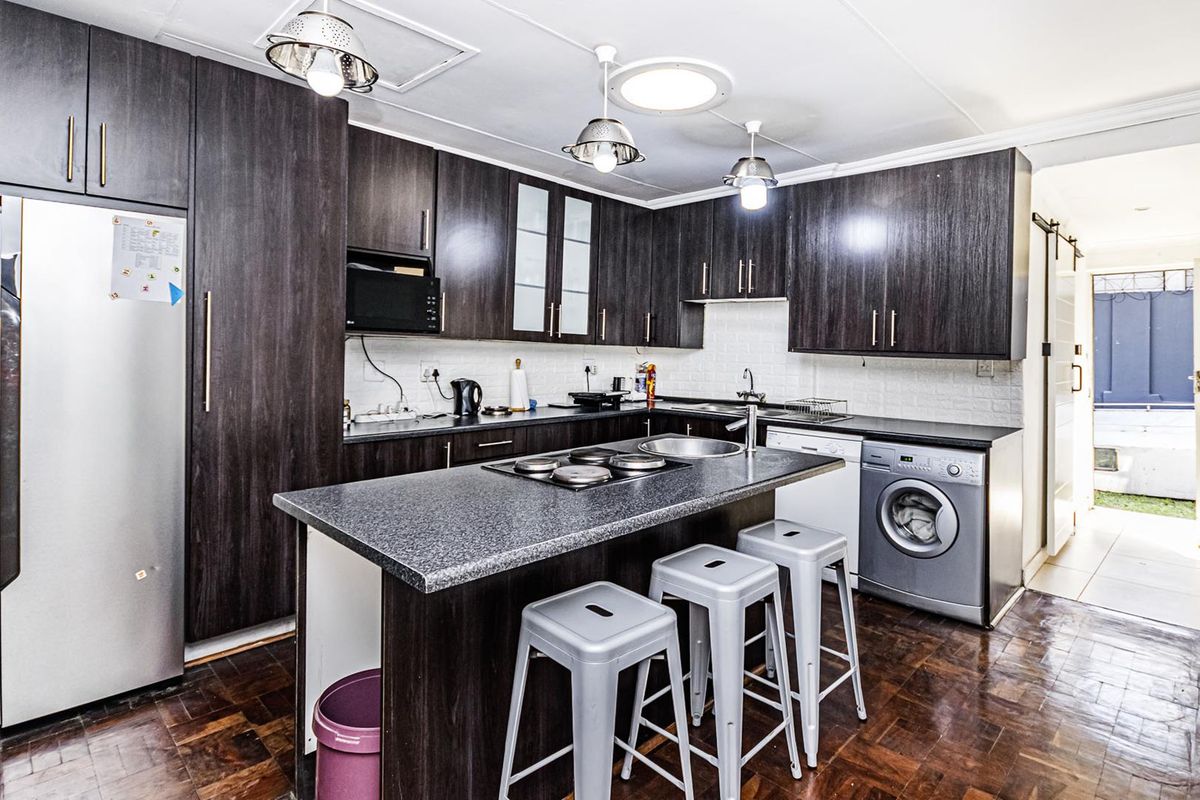 Modern kitchen featuring dark wood cabinetry, granite countertops, a central island with a built-in hob, and parquet flooring.