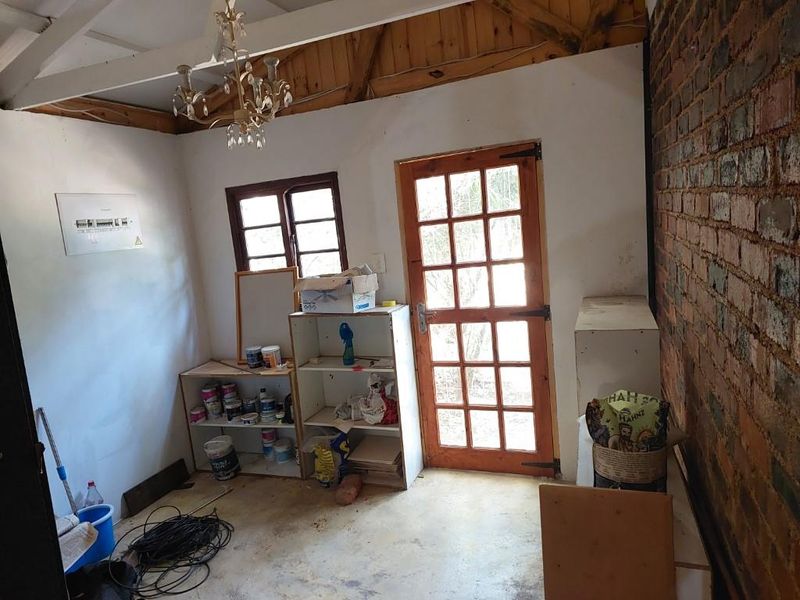 A utility space featuring exposed brickwork, timber ceiling beams, and a timber-framed glass door, offering a rustic foundation for renovation or storage use.