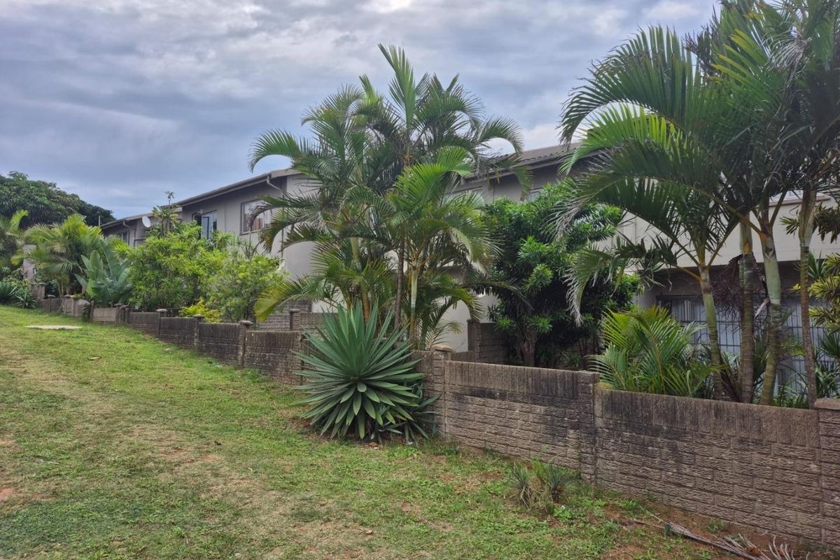 Rear view of the townhouse property featuring a landscaped garden area and a brick boundary wall.