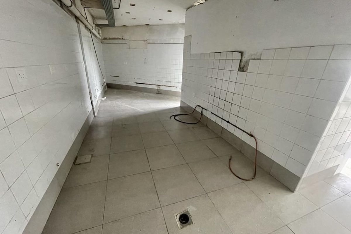 An empty, unfinished utility or kitchen space featuring tiled walls and flooring, requiring significant renovation and completion of fixtures and services.