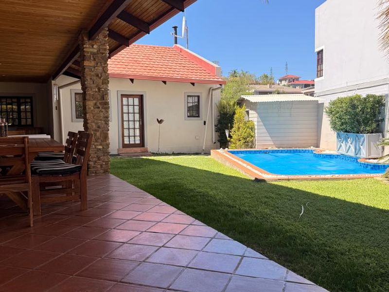 Covered patio area with tiled flooring and timber ceiling, overlooking a private garden with a swimming pool.