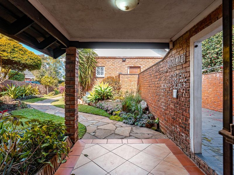 A covered patio area featuring tiled flooring and a brick pillar, overlooking a landscaped garden with a stone paved pathway.
