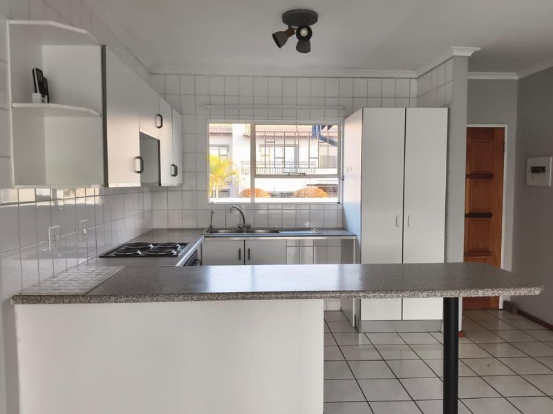 A functional kitchen featuring white cabinetry, laminate countertops, a breakfast bar, and tiled finishes, offering a clean and practical layout.