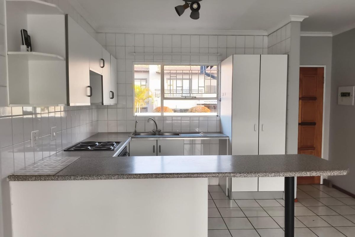 A functional kitchen featuring white cabinetry, laminate countertops, a breakfast bar, and tiled finishes, offering a clean and practical layout.