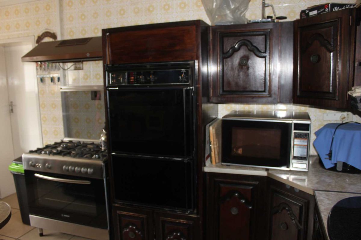A dated kitchen featuring dark wood cabinetry, a built-in double oven, a gas stove with extractor fan, and patterned wall tiling.