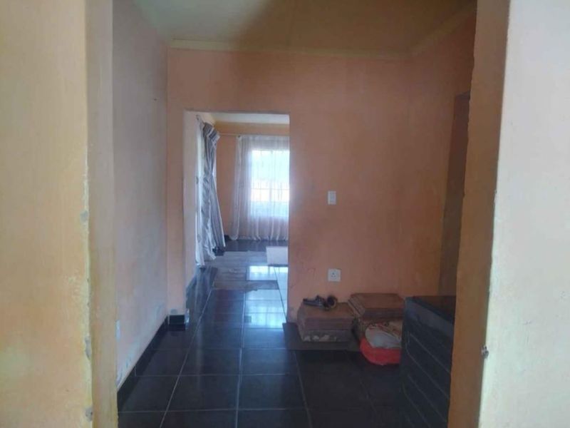A vacant hallway featuring dark tiled flooring and plain wall finishes, providing access to an adjoining room with natural light.