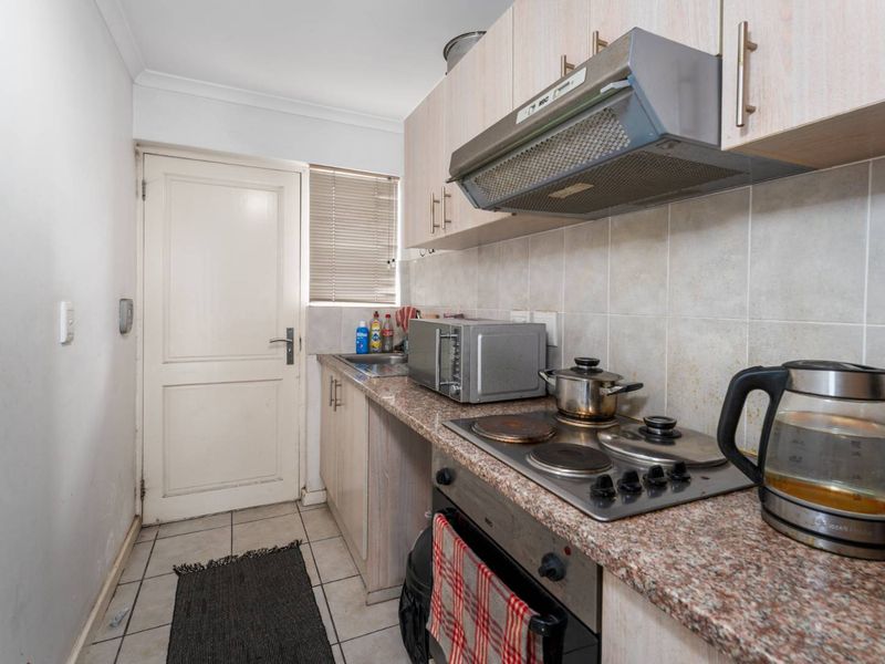 Compact kitchen featuring laminate cabinetry, granite countertops, built-in oven, electric hob, and extractor fan with tiled backsplash and flooring.