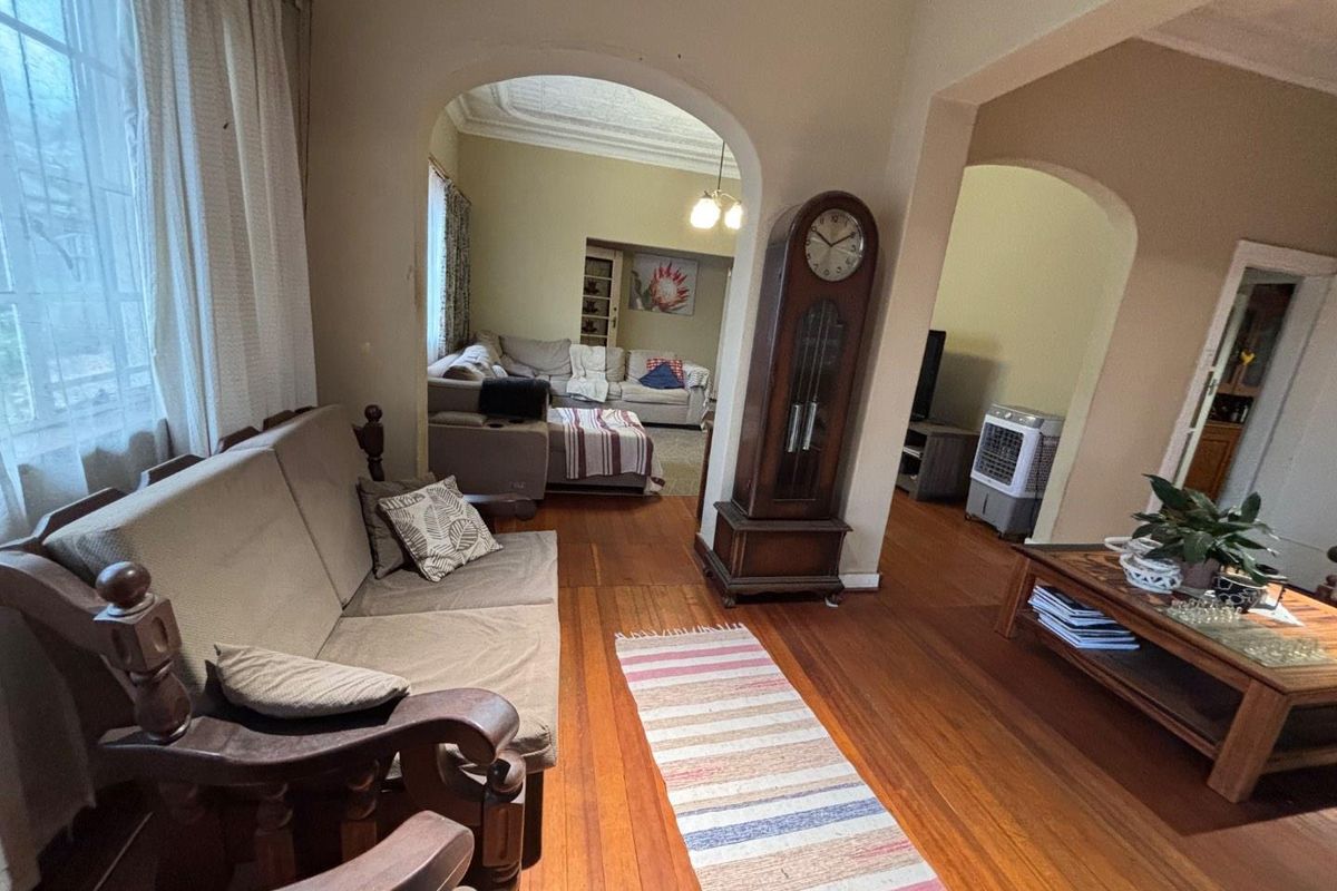 Spacious living area featuring original hardwood flooring, classic arched doorways, and decorative ceiling molding, offering a traditional character feel.