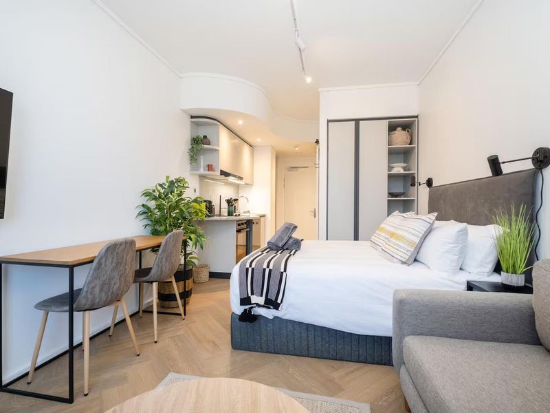 Modern open-plan studio apartment featuring a compact kitchen, built-in storage, and stylish herringbone flooring in a well-maintained living space.