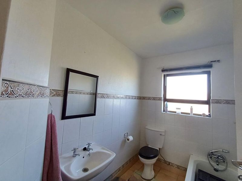 A functional bathroom featuring a pedestal washbasin, toilet, and bathtub with ceramic wall and floor tiling.