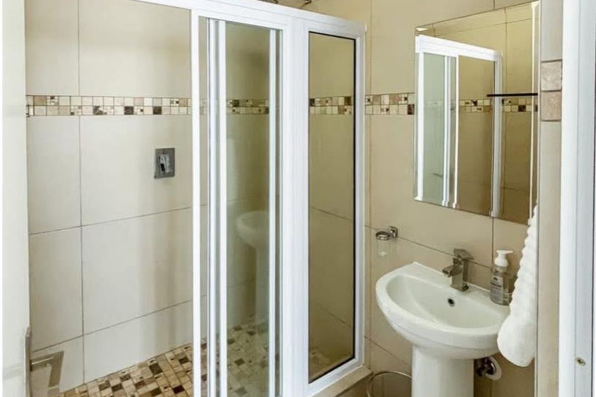 A compact bathroom featuring a tiled shower enclosure with sliding glass doors, a pedestal basin, and a wall-mounted mirror.