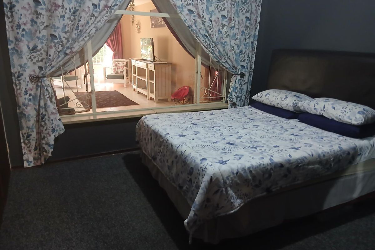 A bedroom featuring a large internal window looking into an adjacent living space, with dark wall finishes and carpeted flooring.