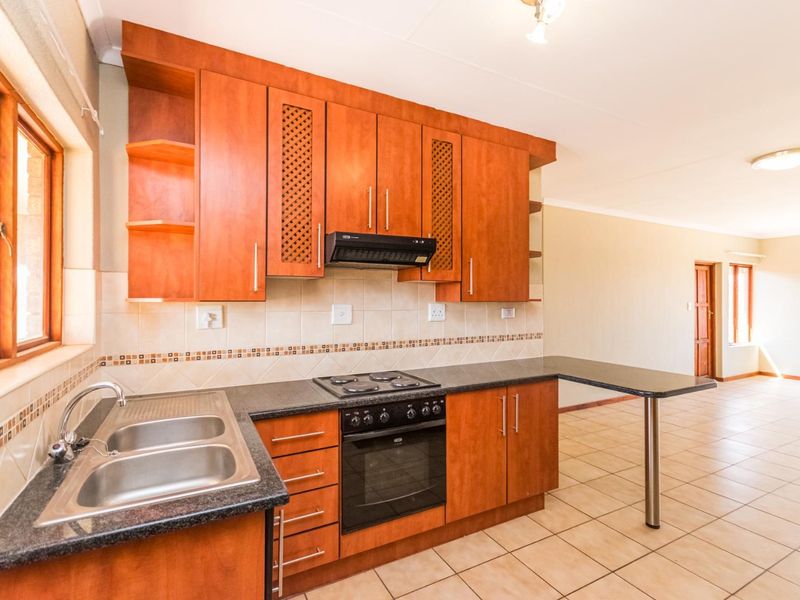 A functional kitchen featuring wooden cabinetry, dark laminate countertops, a built-in oven and hob, and a breakfast bar, opening into an adjacent living area.