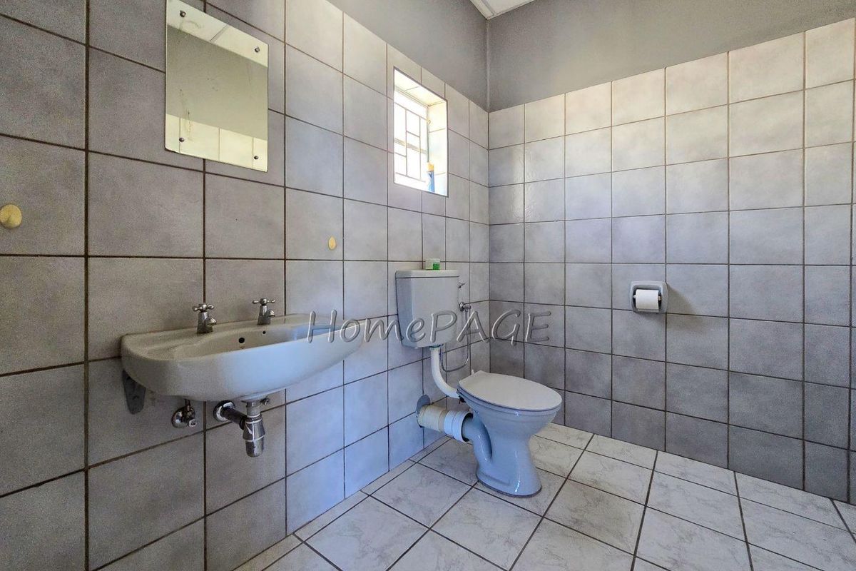 A functional industrial-style bathroom featuring wall-mounted basin, standard toilet, and full-height wall tiling.