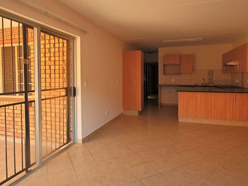 Open-plan living area featuring tiled floors, a functional kitchen with built-in cabinetry and island, and direct access to an outdoor balcony through sliding doors.