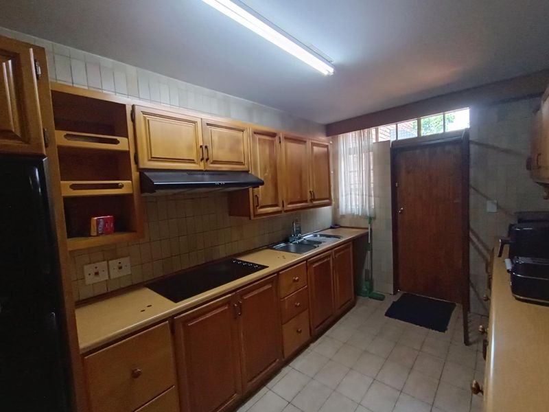 A functional kitchen featuring traditional wooden cabinetry, laminate countertops, a built-in hob with extractor fan, and tiled finishes throughout.