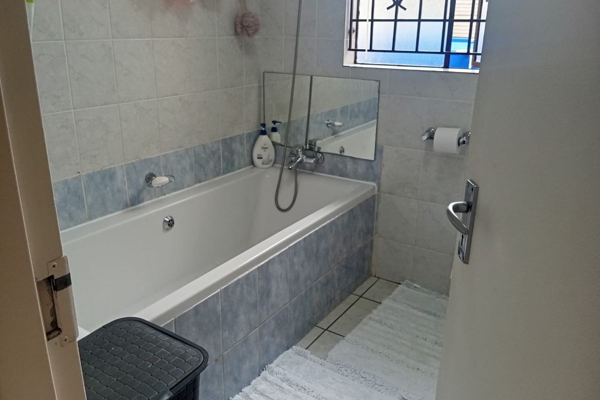 A functional bathroom featuring a built-in bathtub with a handheld shower mixer, tiled walls, and a security-grille window.