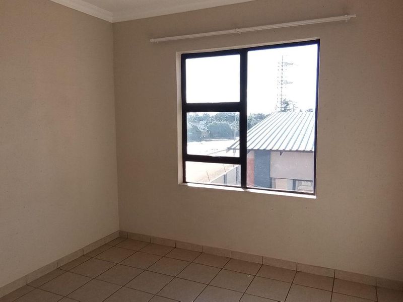 A clean, empty bedroom featuring neutral wall paint, tiled flooring, and an aluminium-framed window with a fitted curtain rod.