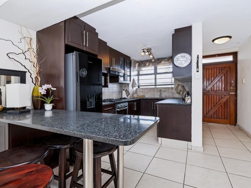 A functional kitchen featuring dark wood cabinetry, granite countertops, a breakfast bar, and integrated appliances, with direct access to the front entrance.