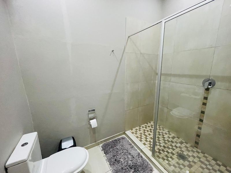 A functional bathroom featuring a glass-enclosed shower with mosaic floor tiling and a standard toilet suite.