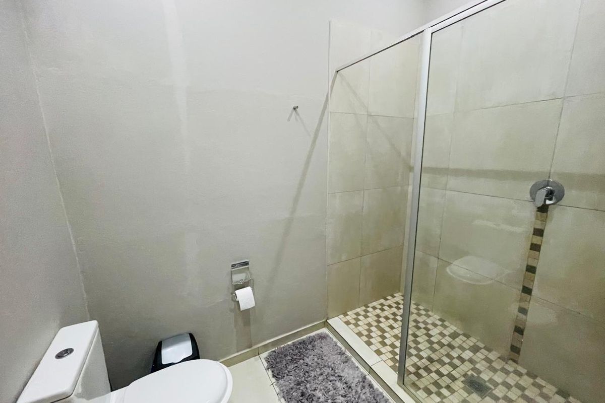 A functional bathroom featuring a glass-enclosed shower with mosaic floor tiling and a standard toilet suite.