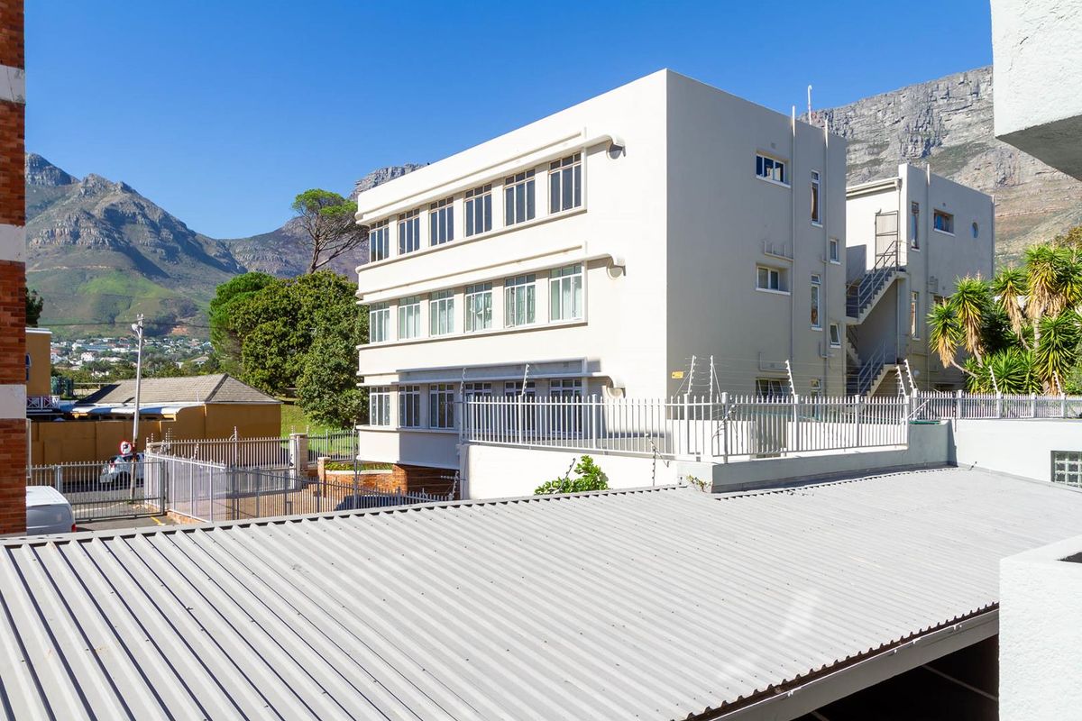 Exterior view of the apartment building featuring a metal roof, external staircase, and secure perimeter fencing against a mountain backdrop.