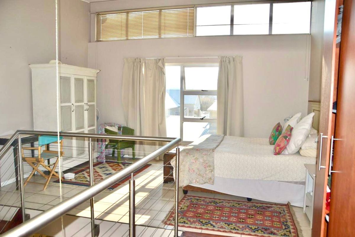 A spacious bedroom featuring high ceilings with clerestory windows, tiled flooring, and a stainless steel balustrade overlooking the lower level.