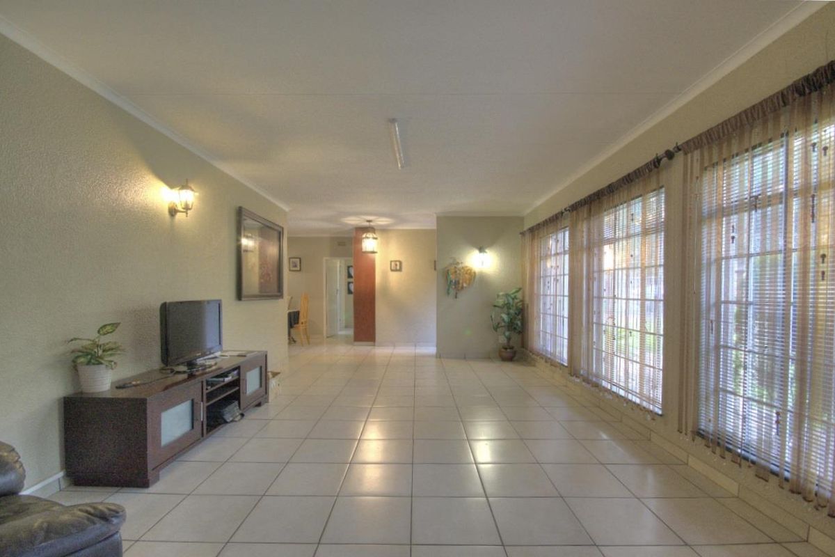 Spacious living area featuring large windows with blinds, tiled flooring, and wall-mounted lighting fixtures.