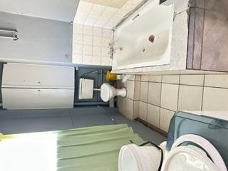 A dated bathroom featuring a built-in bathtub, toilet, and storage cabinetry, requiring significant renovation and cosmetic updates to improve functionality and aesthetic appeal.
