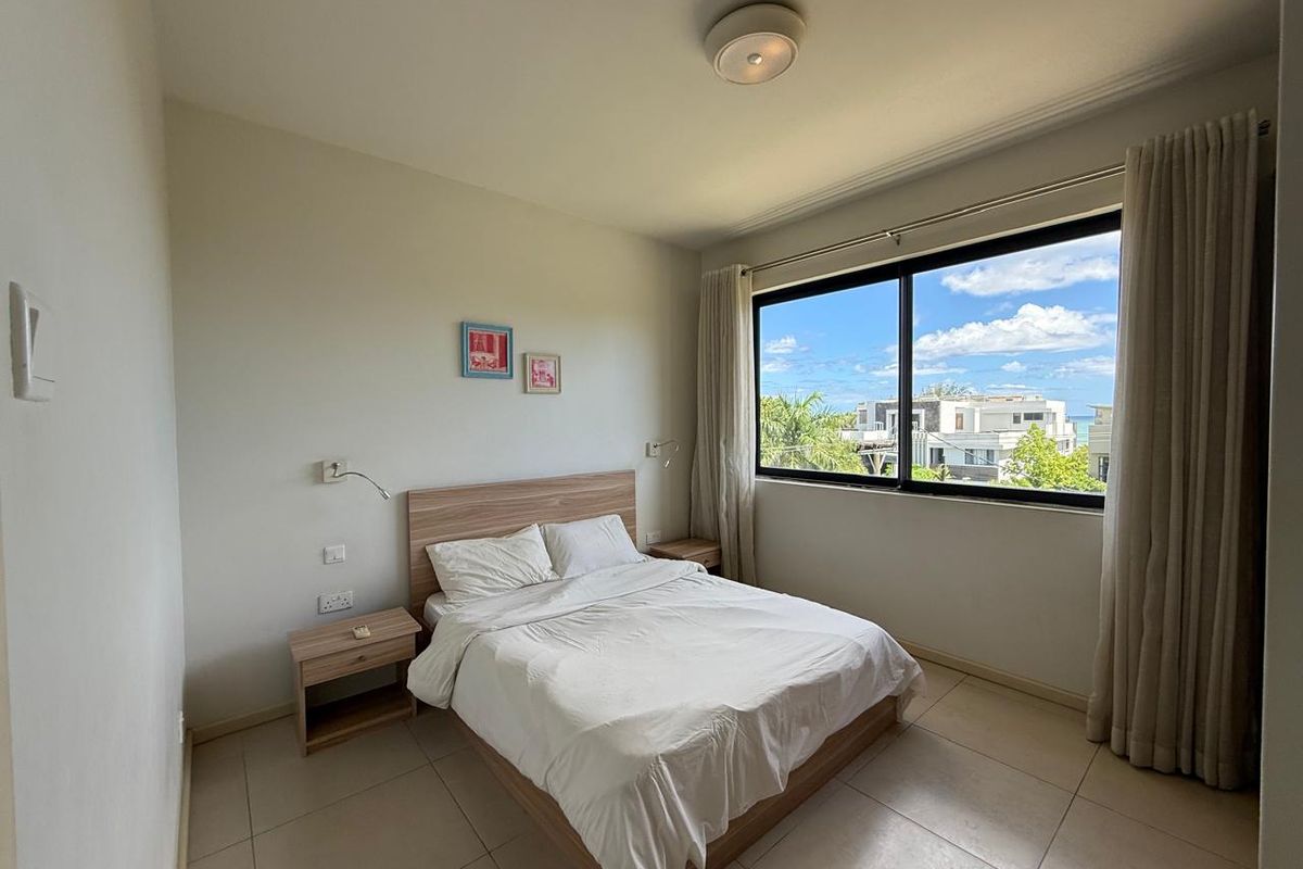 A bright bedroom featuring tiled flooring, a large window with natural light, and a view of the surrounding neighborhood.