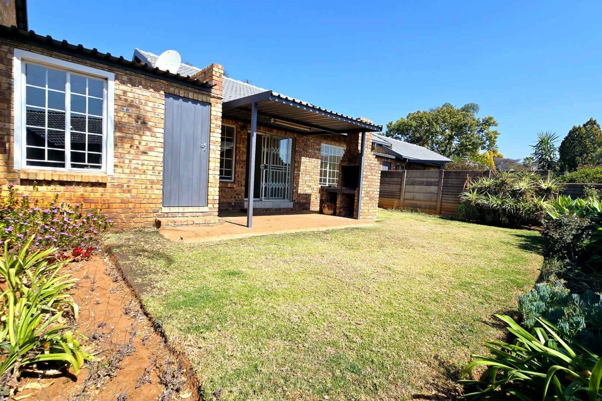 A private rear garden featuring a paved patio area with a built-in braai, brick exterior walls, and a well-maintained lawn.