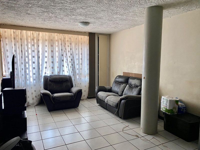 Living room featuring ceramic floor tiles, a prominent structural column, and textured ceiling, offering a blank canvas for potential renovation and modernization.