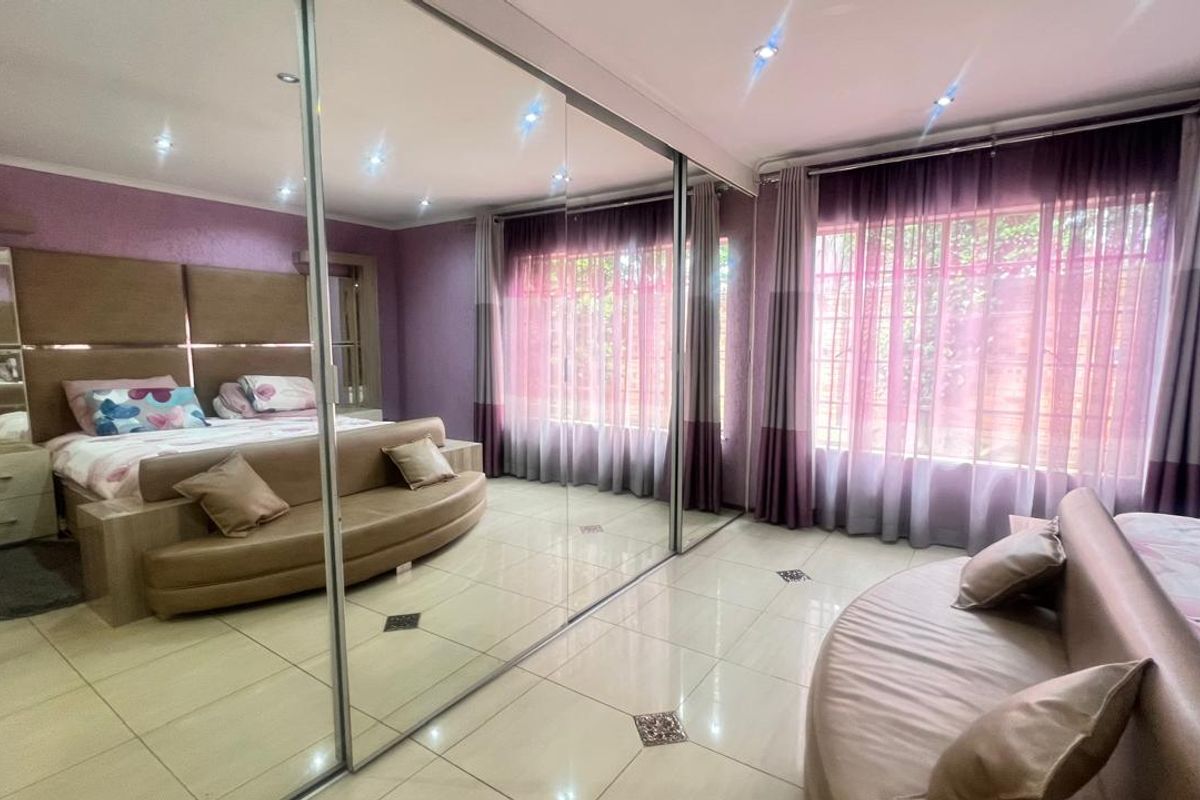 Spacious bedroom featuring large floor-to-ceiling mirrored sliding wardrobe doors, tiled flooring, and recessed downlighting.