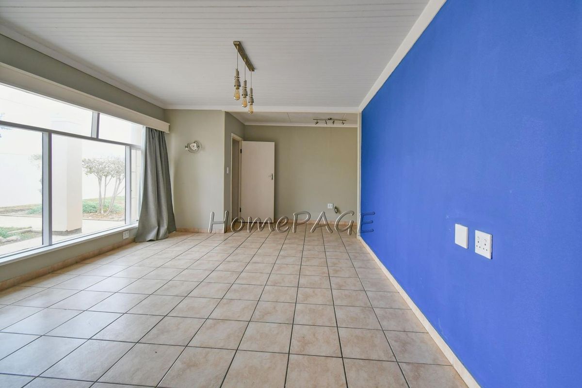 A spacious, empty living room featuring large windows, tiled flooring, and a prominent blue accent wall, offering a blank canvas for interior design.