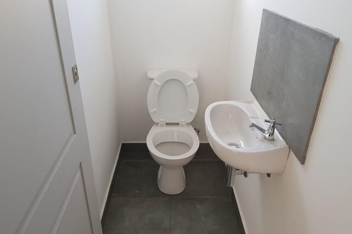 A compact industrial-style powder room featuring a wall-mounted basin, modern toilet, and dark floor tiling.