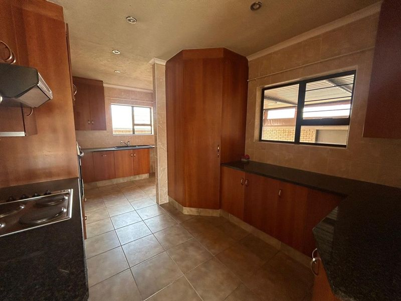 A spacious kitchen featuring extensive wooden cabinetry, granite countertops, integrated hob, extractor fan, and tiled flooring with ample natural light.