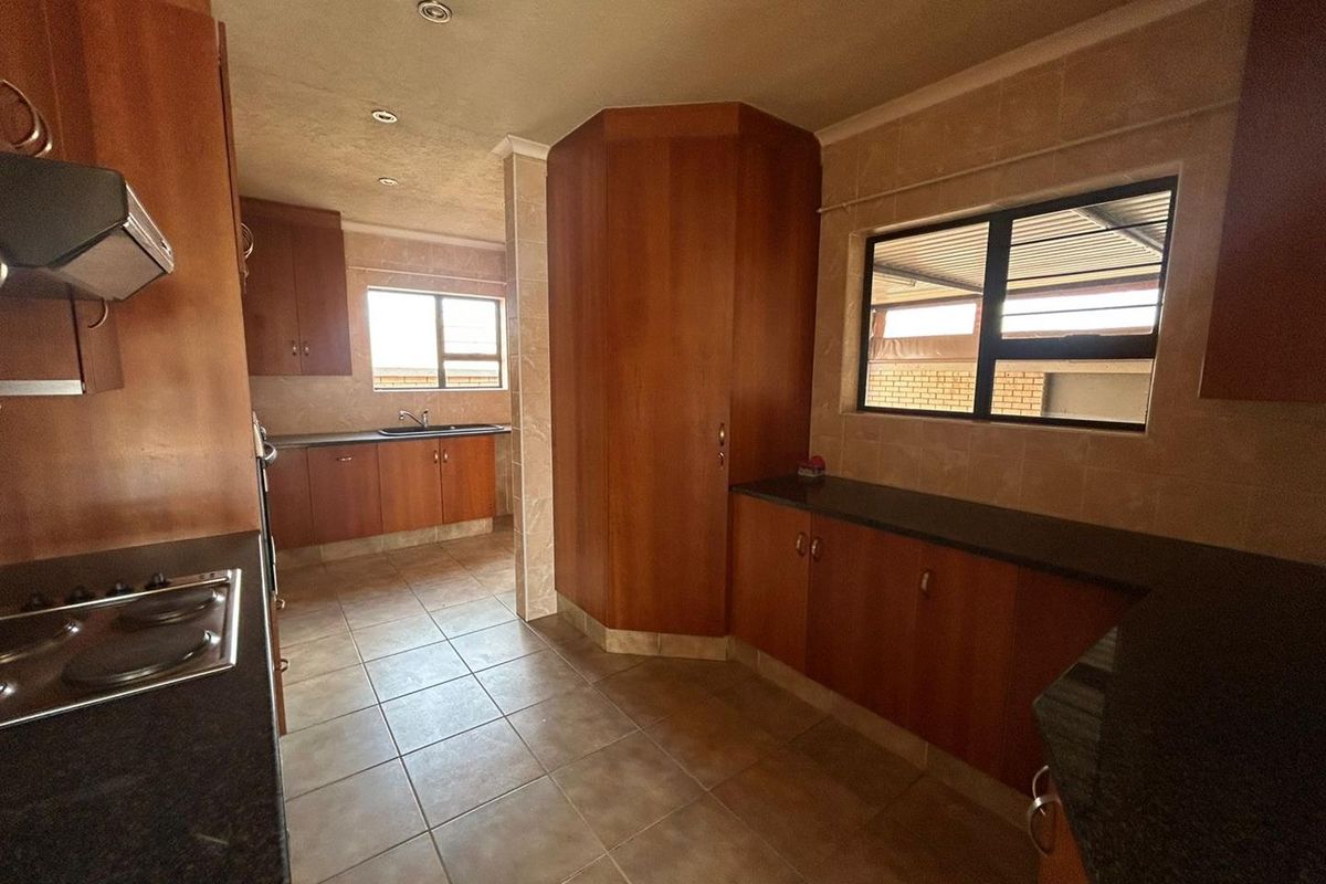 A spacious kitchen featuring extensive wooden cabinetry, granite countertops, integrated hob, extractor fan, and tiled flooring with ample natural light.