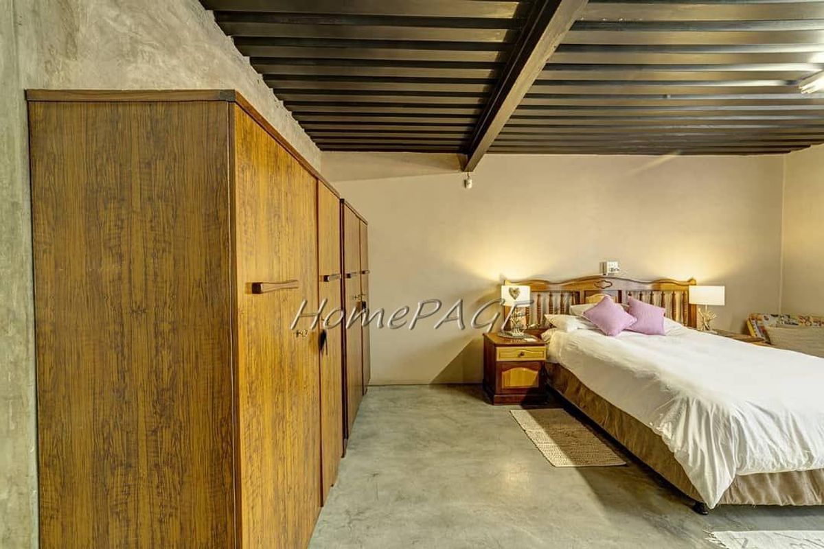 A bedroom featuring exposed industrial-style ceiling beams, concrete flooring, and built-in wooden cabinetry.